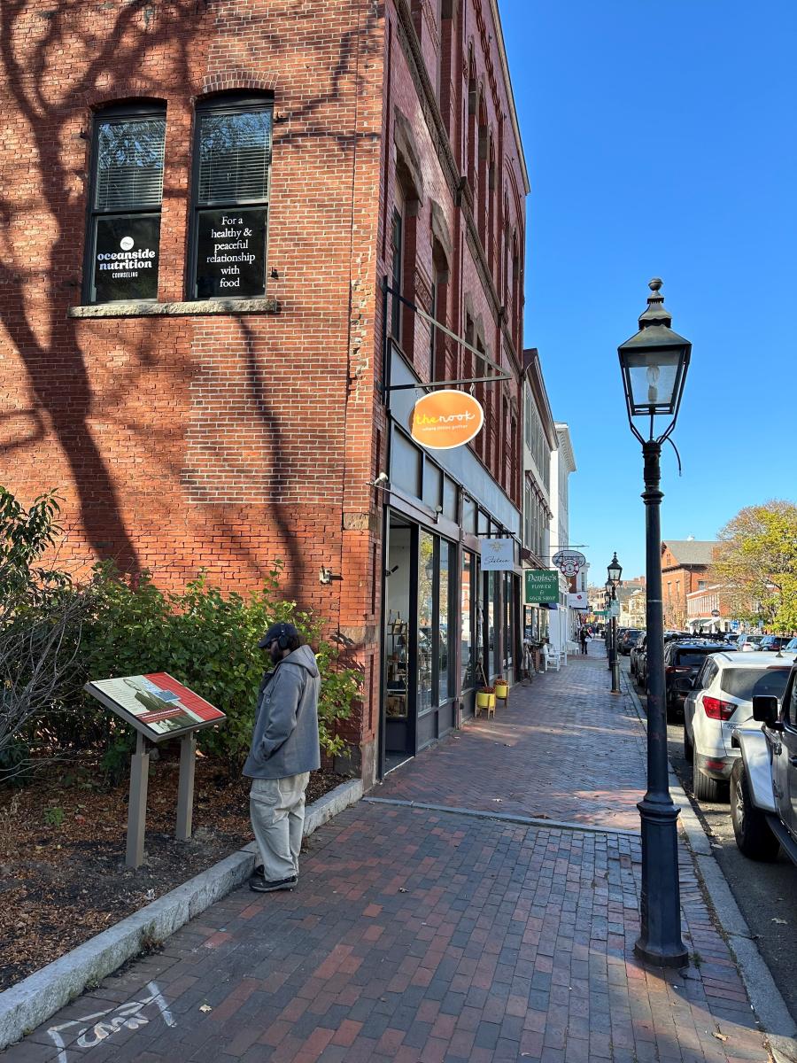 •	Man reading “Perseverance in a Precarious World” interpretive sign about Louis C. Tyree on Pleasant St. (photo by Geordie Vining, 11/17/2023)
