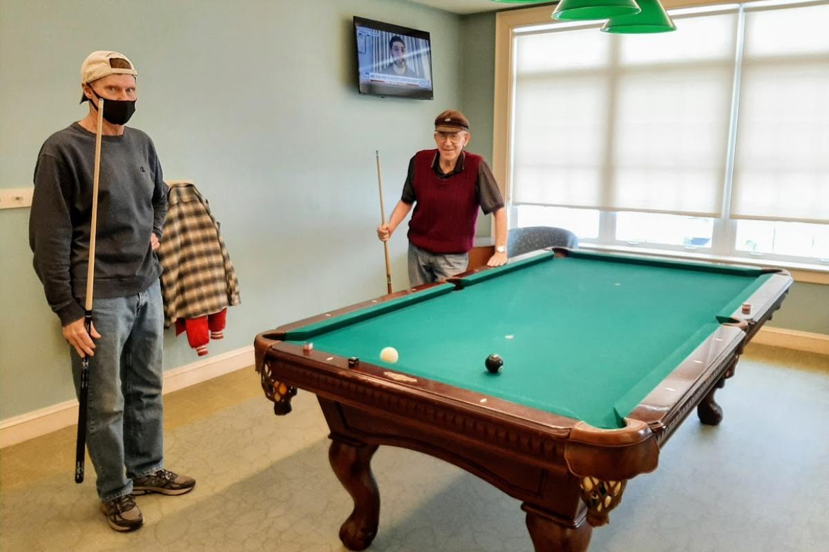 Two men stand next to the pool table that they are about to clear