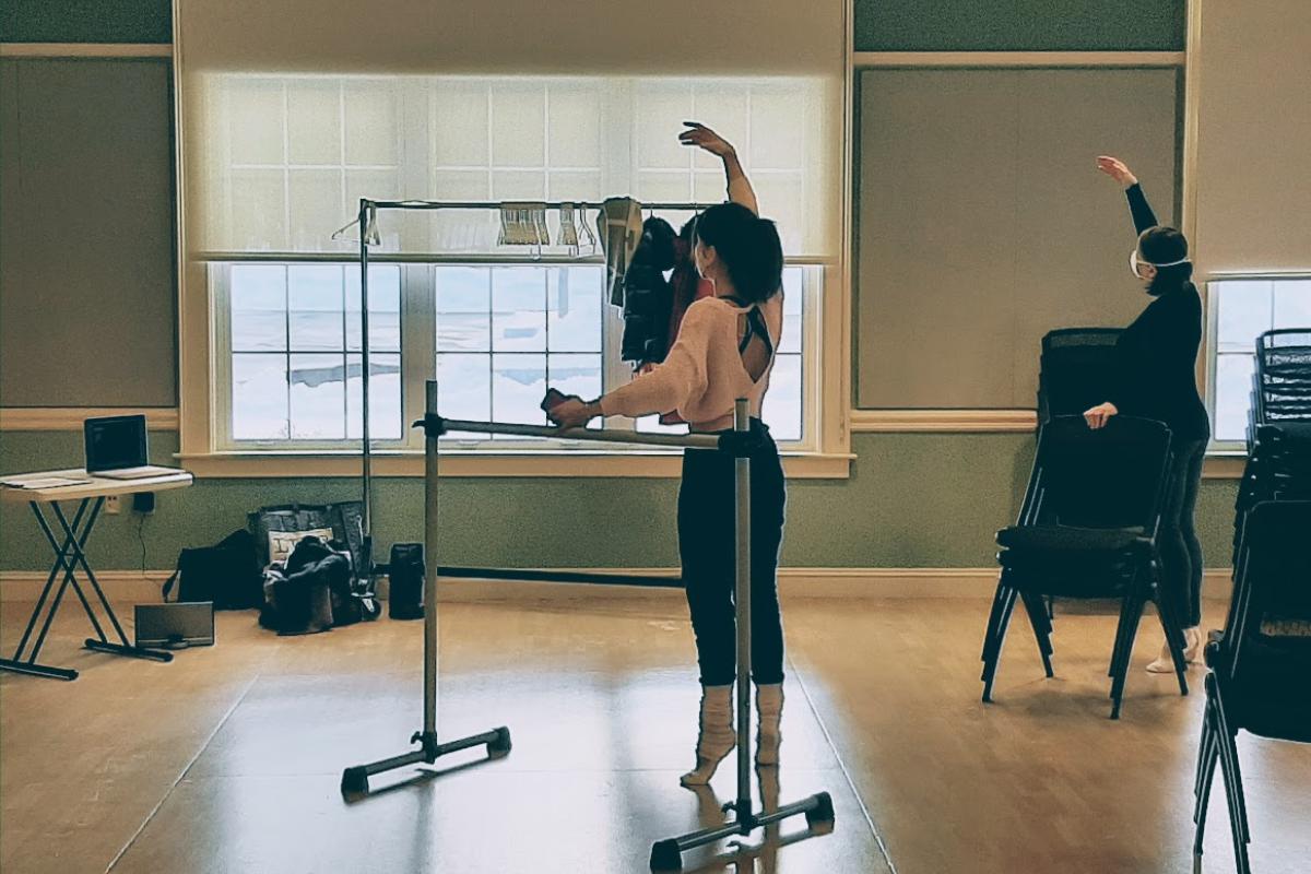 Two ballet dancers are on their toes with an arm raised