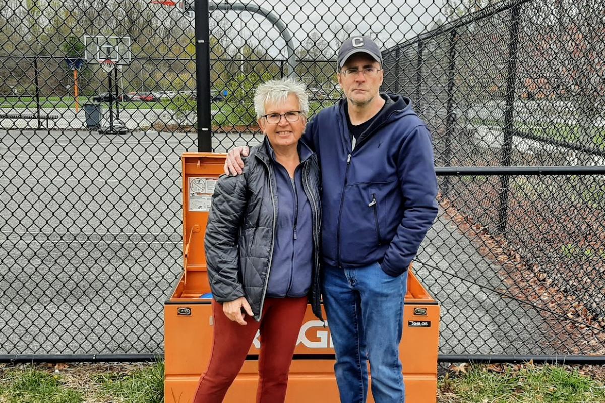 A woman and man stand in front of a large metal orange box next to basketball court