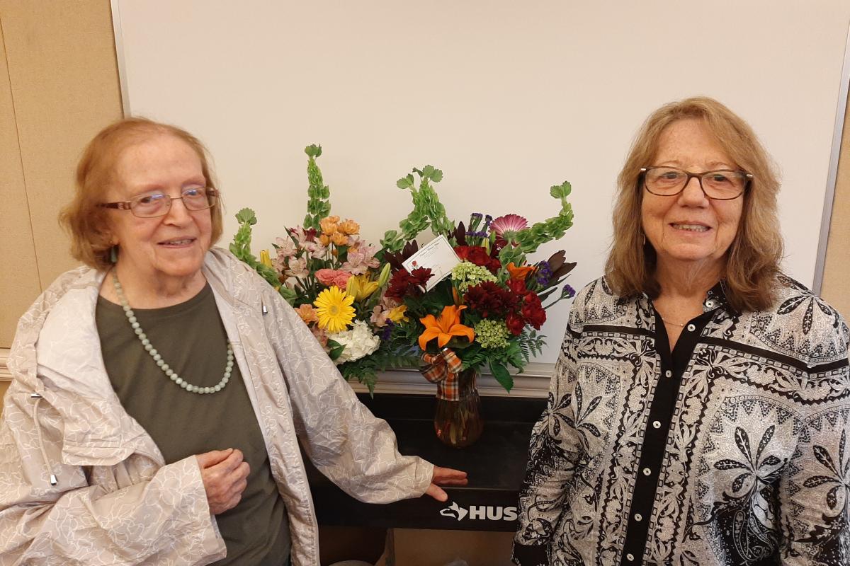 Two smiling women stand in front of beautiful floral arrangements