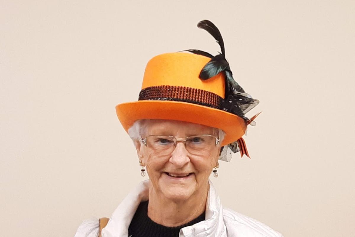 A woman wears an orange hat with a tall black feather