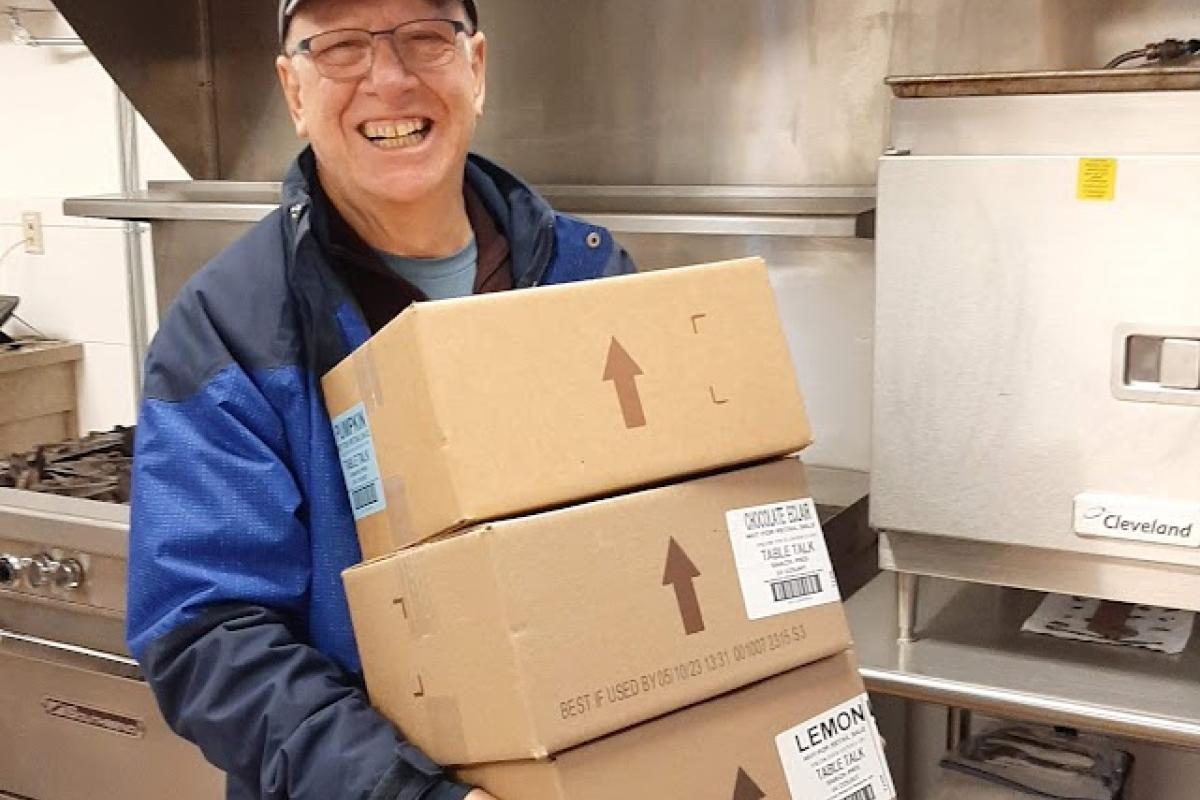 A man carries three large boxes in a commercial kitchen
