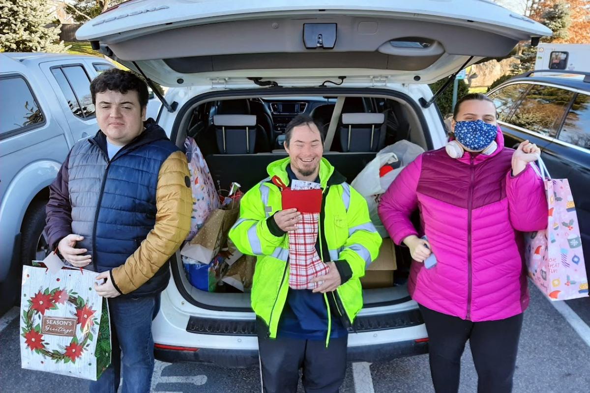 Three people holding holiday bags stand behind an open hatchback