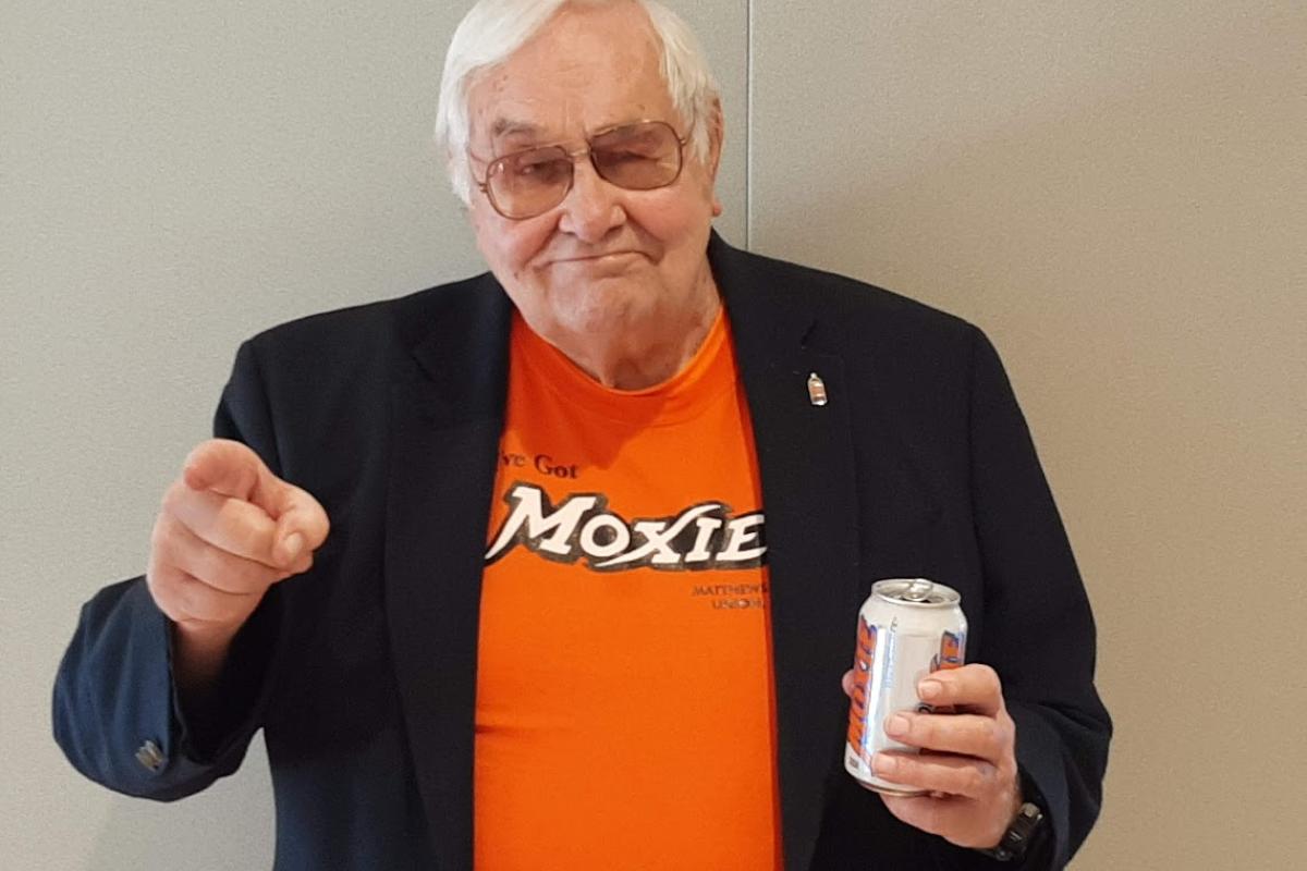  A man wearing an orange Moxie shirt points forward