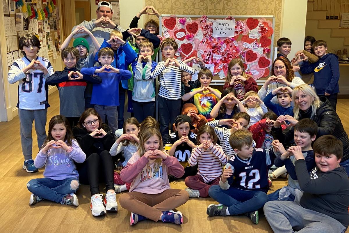 A group of mostly children sit in front of a Valentine's Day display