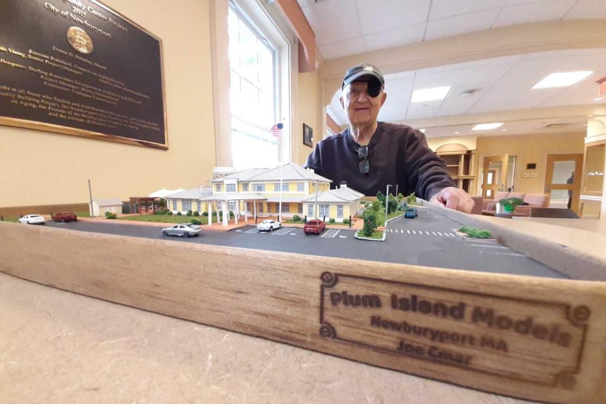 A man stands behind a miniature model of a building and grounds