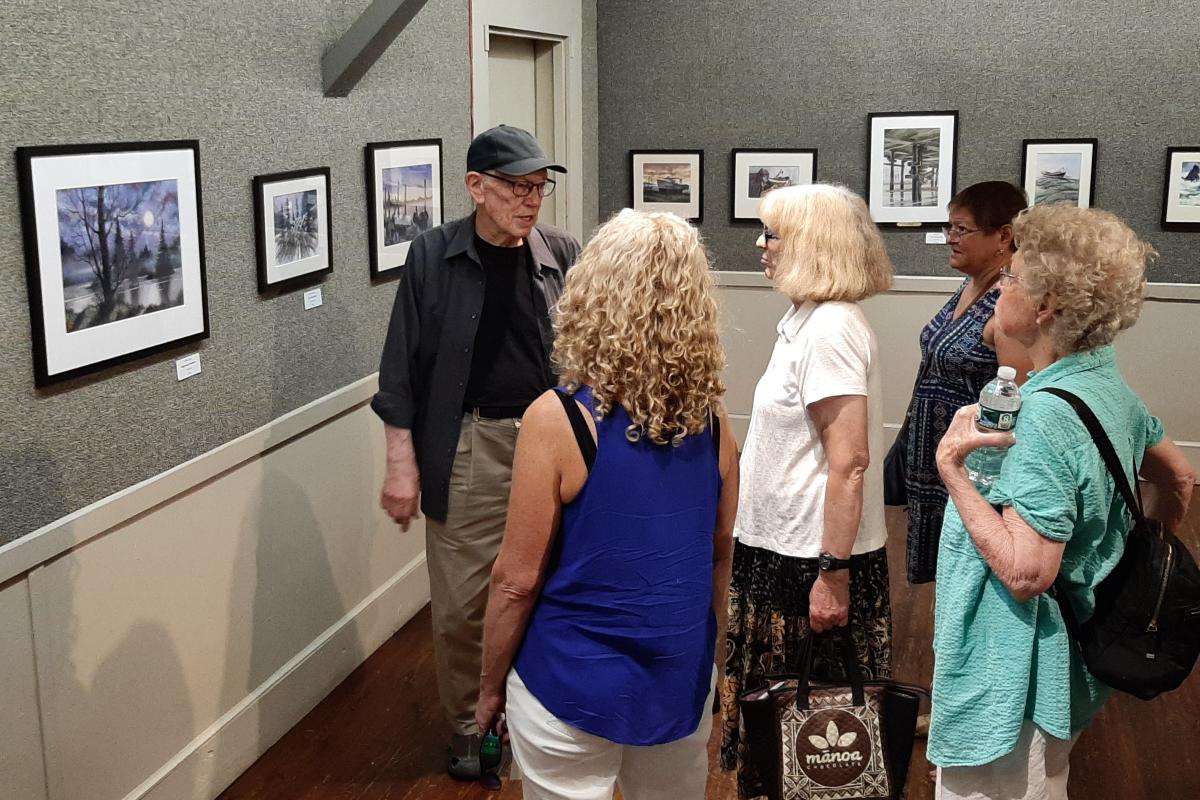 A group of woman pay close attention to a man speaking in an art gallery