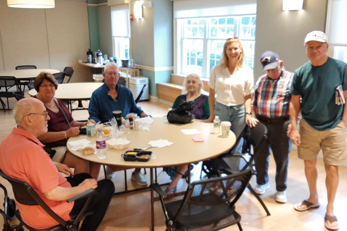A group of 8 people both sitting a standing pose for a photo in a lunch room