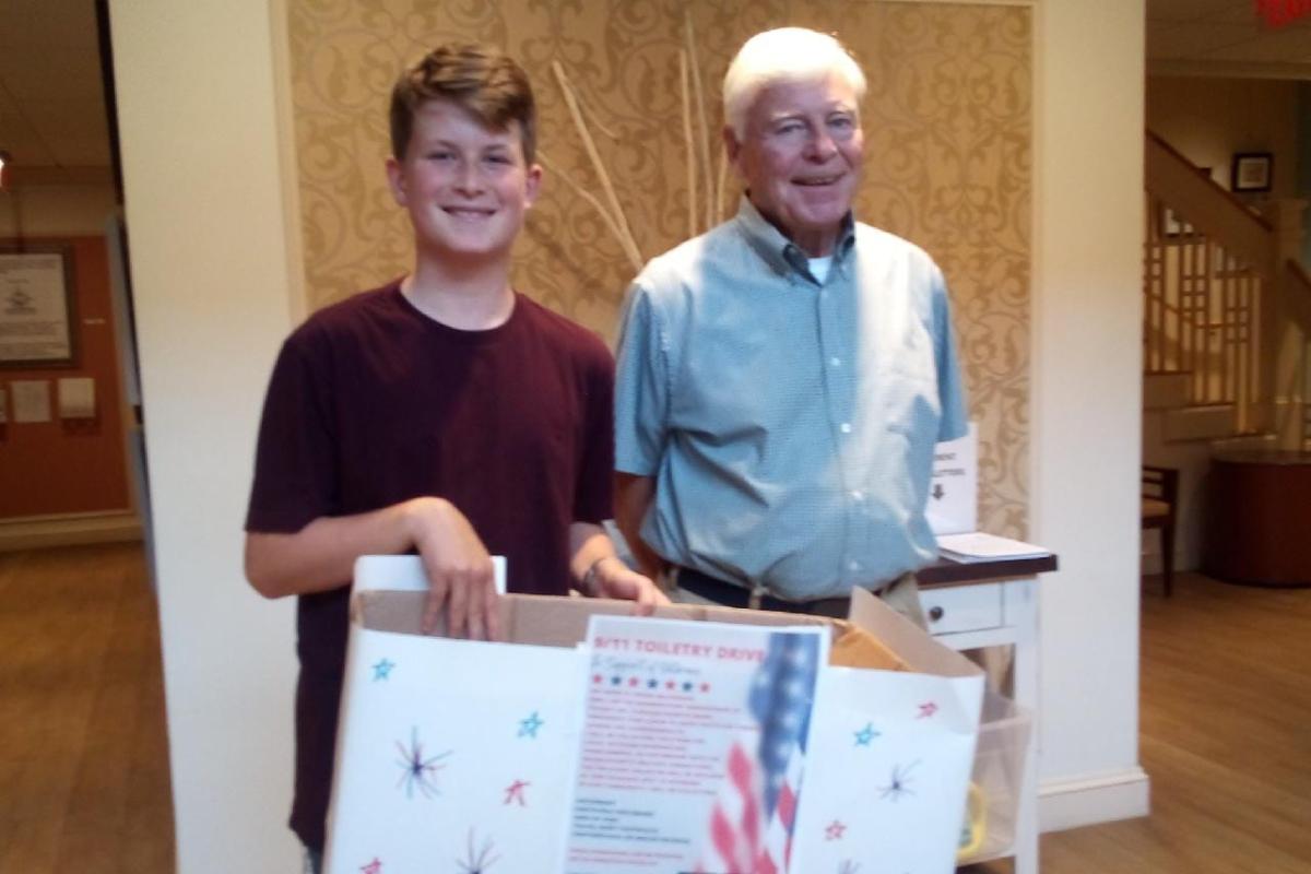 A boy holding a donation box stands next to an older man