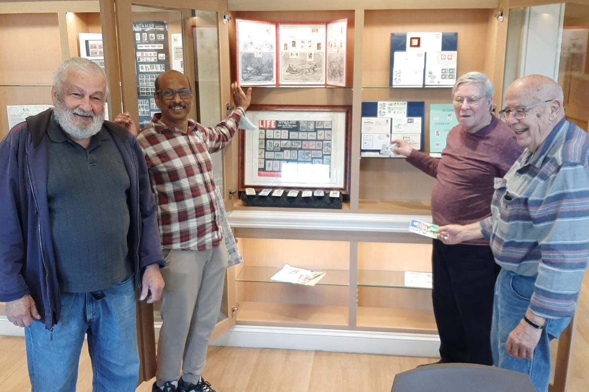 Four men stand in front of a display case they are adding to