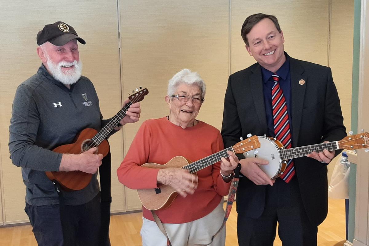 Three people play ukulele while standing
