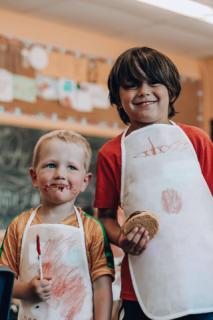 two boys with aprons and cookies and chocolate on their face